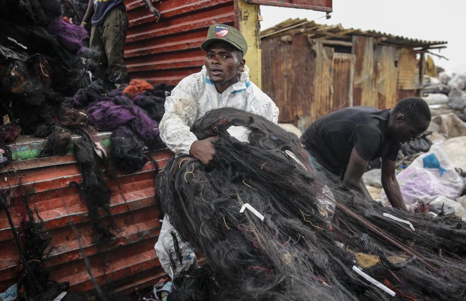 A man scavenges for artificial hair at Dandora, the largest garbage dump in the Kenyan capital of Nairobi, on Sunday, March 28, 2021. He is wearing a protective medical suit that he and his friends had found thrown away by hospitals. Trash pickers, who are not eligible for the COVID-19 vaccine, say the gear protects them from the weather during the rainy season. (AP Photo/Brian Inganga)