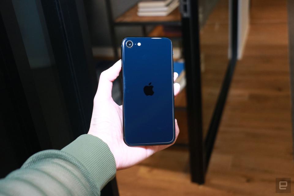 <p>A hand holding the iPhone SE (2022) under a spotlight with its rear facing the camera. It's a shade of deep blue.</p>
