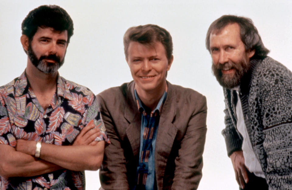George Lucas, David Bowie, and Jim Henson posing together, each smiling and looking directly at the camera