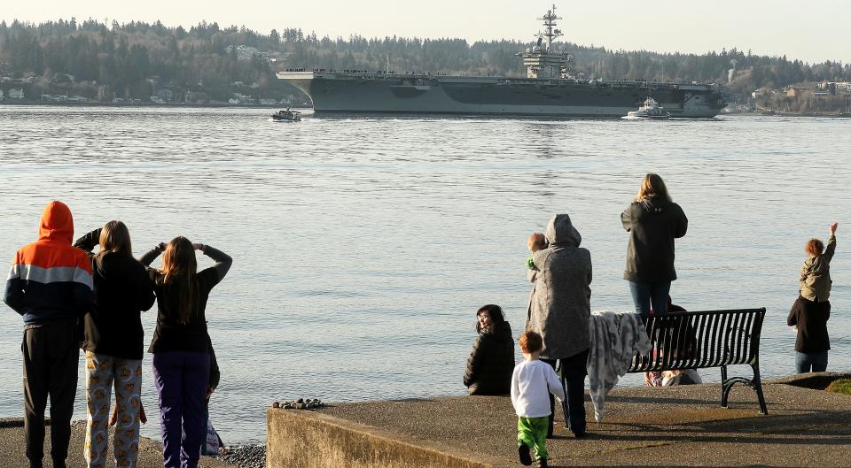 Family and friends of the sailors aboard the USS Theodore Roosevelt (CVN-71) wave from the shore of Bachmann Park in Bremerton, Wash. as the aircraft carrier departs Puget Sound Naval Shipyard after its 18-month overhaul, on Friday, March 17, 2023.