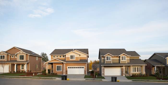 Two suburban houses with landscaped lawns, garages, and driveways are shown on a quiet residential street. The sky is clear