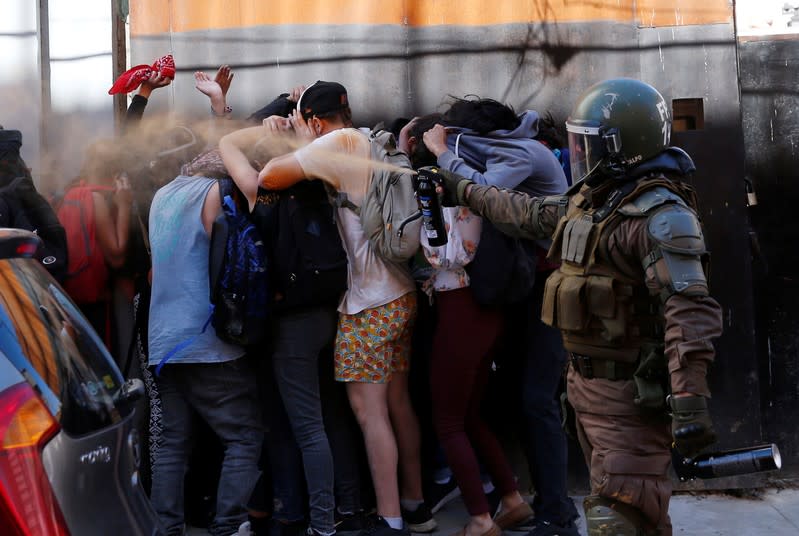 Un miembro de las fuerzas de seguridad usa gas pimienta mientras los manifestantes se cubren durante una protesta contra el gobierno de Chile en Valparaíso, Chile.