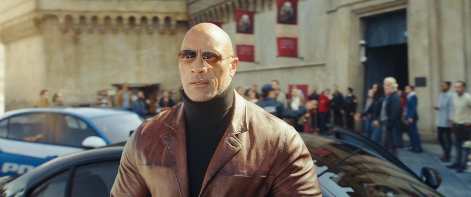 Dwayne Johnson in a leather jacket, black turtleneck, and glasses