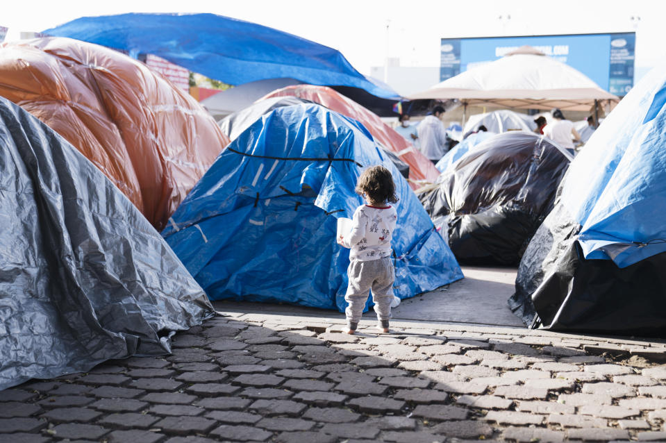 A child walks past tents at a makeshift housing camp for migrants seeking asylum hearings in Tijuana, Mexico, on Sunday, March. 21, 2021. / Credit: Eric Thayer/Bloomberg via Getty Images