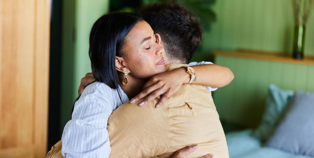 young woman hugging her husband while at home sitting on their bed