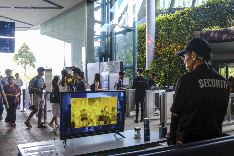 In this March 14, 2020, photo, a security personnel views a thermal screening monitor as visitors enter Gardens by the Bay in Singapore. As the virus outbreak spreads ever further, it's becoming clear that some strategies are more likely to succeed in containing it: pro-active efforts to track down and isolate cases, access to basic, affordable public health and clear, reassuring messaging from leaders. (AP Photo/Ee Ming Toh)