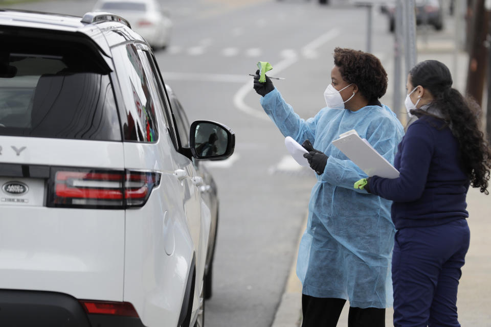 Dr. Jacqueline Delmont, Chief Medical Officer of Somos Community Care, left, holds up an armband that signifies the client has tested positive for coronavirus antibodies at a drive-through testing site in Hempstead, N.Y., Tuesday, April 14, 2020. The test takes approximately 15 minutes and looks for the presence of antibodies in a person's blood, signifying that they may have some immunity to the coronavirus. (AP Photo/Seth Wenig)