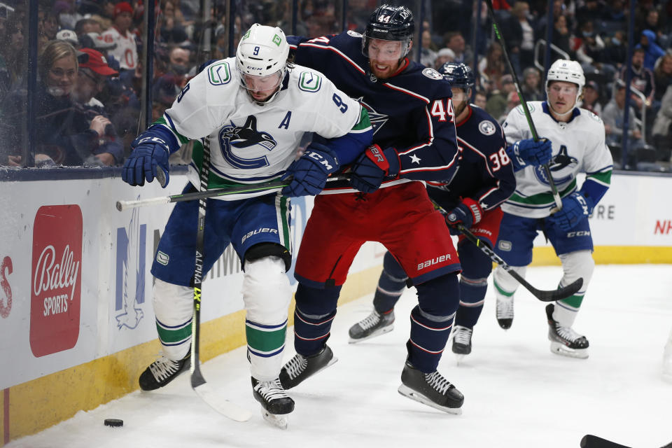 Vancouver Canucks' J.T. Miller, left, tries to clear the puck away from Columbus Blue Jackets' Vladislav Gavrikov during the first period of an NHL hockey game Friday, Nov. 26, 2021, in Columbus, Ohio. (AP Photo/Jay LaPrete)