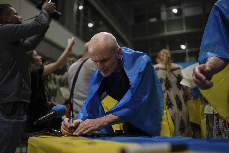 Valeriy Matiushenko, quien pasó siete años retenido por Rusia, firma una bandera nacional ucraniana en el aeropuerto de Kiev, Ucrania, el 29 de junio de 2024. Diez ucranianos que llevaban años retenidos fueron liberados de su cautiverio ruso con la mediación del Vaticano, según el presidente de Ucrania, Volodymyr Zelenskyy. (AP Foto/Alex Babenko)