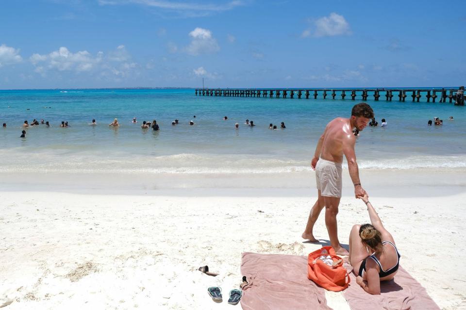 A man holds a woman's hand on a white beach with calm seas and sky