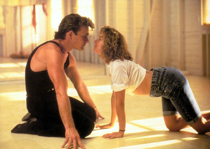 Patrick Swayze in a black tank top and Jennifer Grey in a casual outfit, both performing a dance routine on the floor, facing each other closely