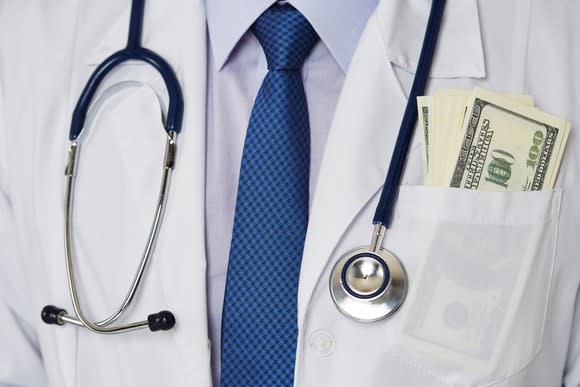 Closeup of physician's lab coat, stethoscope, and blue tie, with hundred dollar bills in his pocket.