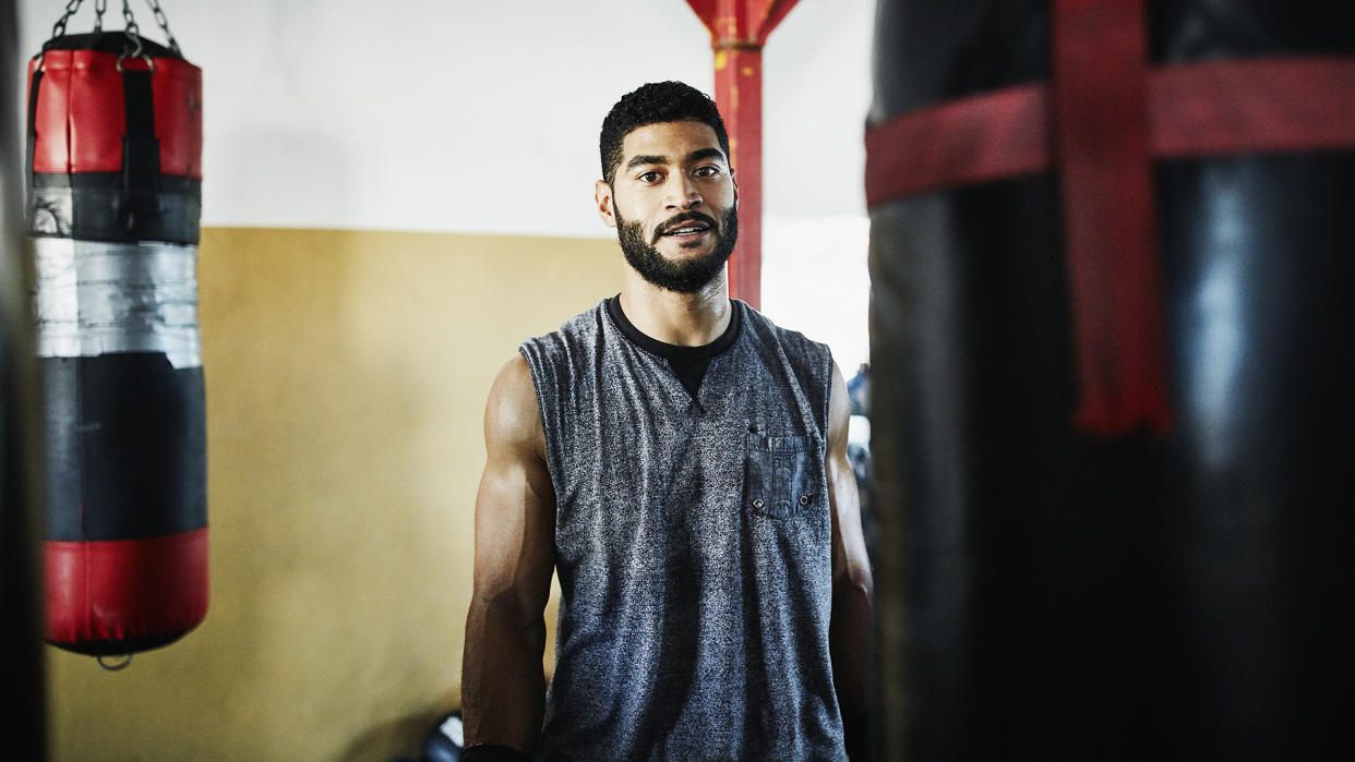  Get fit 2024: Portrait of male boxer standing by heavy bag in boxing gym. 