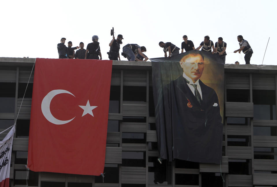 Police hang a banner of Mustafa Kemal Ataturk, founder of the modern Turkey, next to a Turkish flag hung by protesters in a cultural center during a police operation to evacuate Taksim Square in Istanbul Tuesday, June 11, 2013. Hundreds of police in riot gear forced through barricades in the square early Tuesday, pushing many of the protesters who had occupied the square for more than a week into a nearby park. (AP Photo/Thanassis Stavrakis)