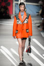 <p><i>Model wears an orange coat with graphic, comic-book images from the SS18 Prada collection. (Photo: ImaxTree) </i></p>