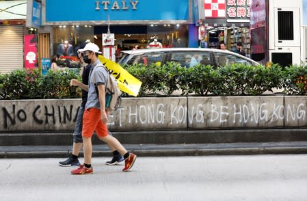 Protesters carry a banner as they walk past the graffiti, during a demonstration to support the city-wide strike and to call for democratic reforms in Mong Kok area in Hong Kong