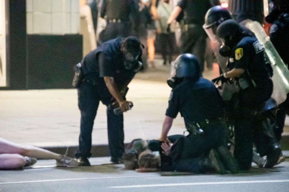 An officer is seen spraying a substance toward a person being detained by police officers during a protest in downtown Detroit on August, 23, 2020.