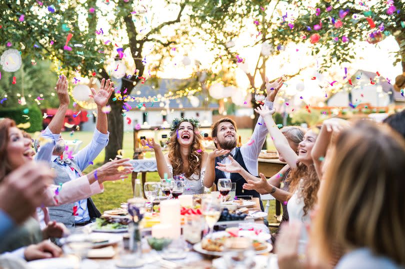 Wedding reception outside in the backyard. Bride and groom with family and guests sitting around the table, having fun.