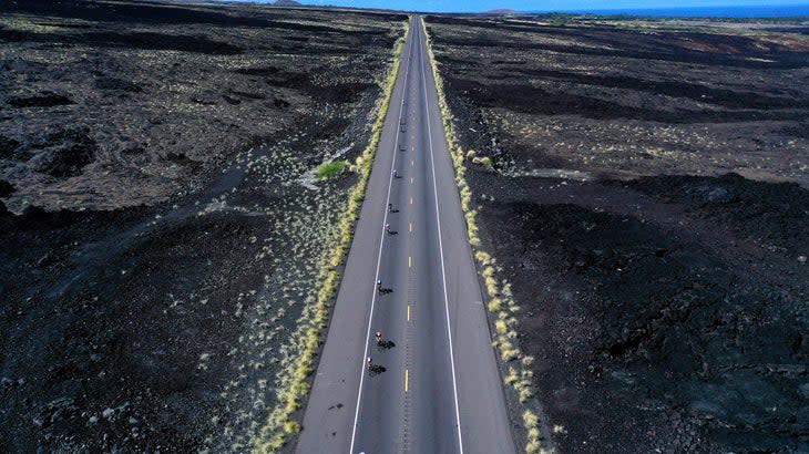 Cyclists on a long road through black lava fields