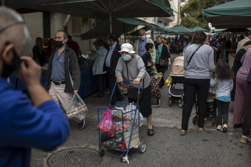 People wearing face masks to curb the spread of coronavirus walk at an open air fruit and vegetable market in Petralona district of Athens, on Wednesday, Nov. 4, 2020. Greece, on Tuesday reported a new record of over 2,000 daily COVID-19 infections, and a further 13 deaths – which bring the overall death toll to over 650. (AP Photo/Petros Giannakouris)