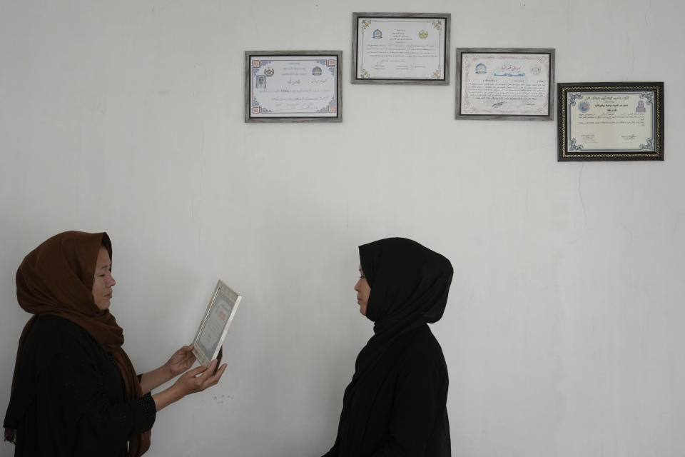 Sisters of 20-year-old Vahida Heydari, a victim of a suicide bomber attack on a Hazara education center, look at one of her educational certificates in their home, in Kabul, Afghanistan, Sunday, Oct. 2, 2022. Last week’s suicide bombing at the Kabul education center killed as many as 52 people, more than double the death toll acknowledged by Taliban officials, according to a tally compiled by The Associated Press on Monday. (AP Photo/Ebrahim Noroozi)