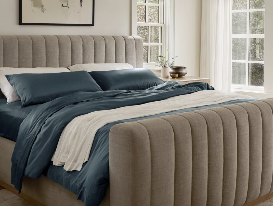 Blue Cozy Earth bedsheets on a fully made bed with a taupe headboard. 