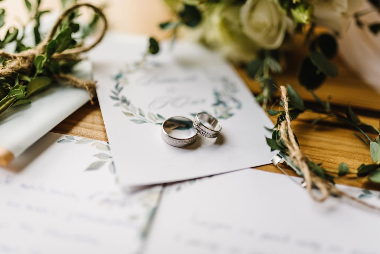 Two silver wedding bands on a white floral wedding invitation