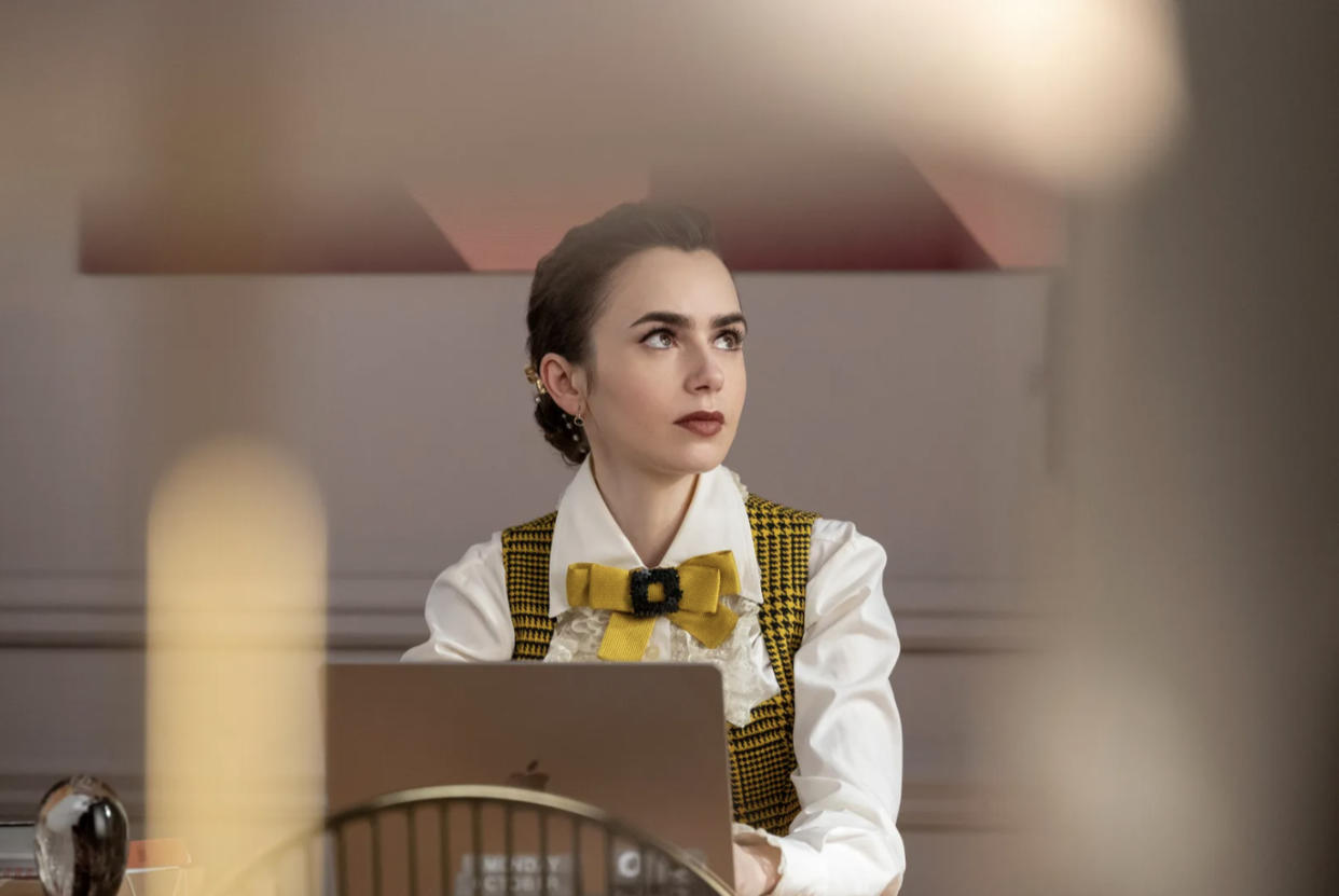 Lily Collins sits in front of a laptop computer in the series Emily in Paris.