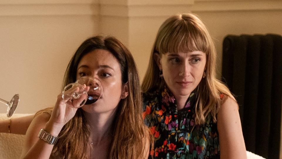 Margot drinking a glass of wine with Candela looking concerned.