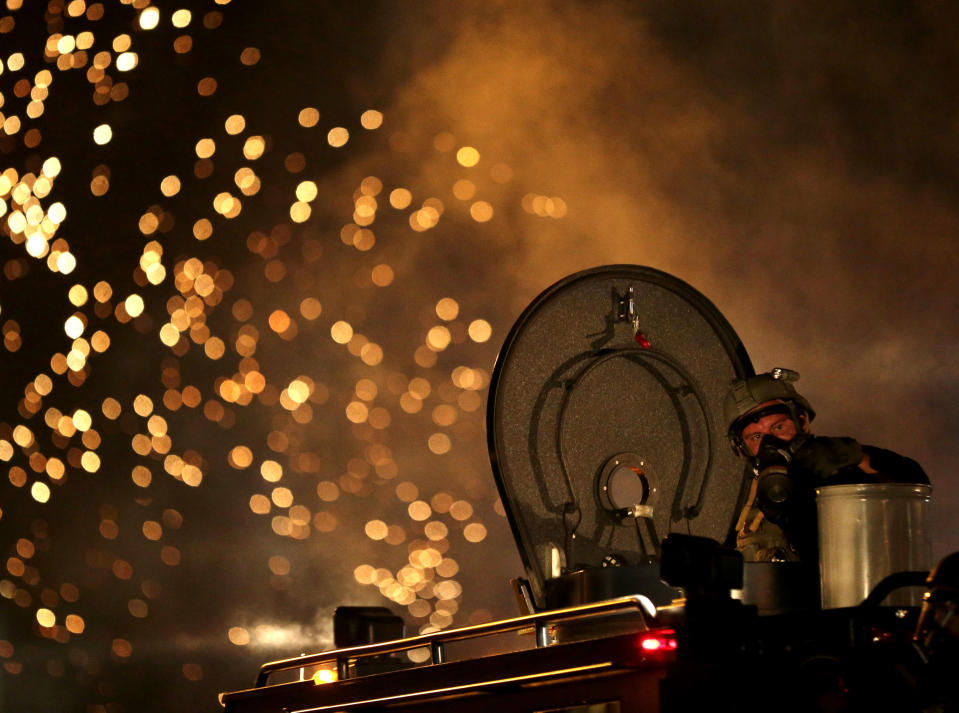 <p>A law enforcement officer on a tactical vehicle watches after a device was fired to disperse a crowd on August 17, 2014, during a protest for Michael Brown, who was killed by a police officer last Saturday in Ferguson, Mo. As night fell in Ferguson, another peaceful protest quickly deteriorated after marchers pushed toward one end of a street. Police attempted to push them back by firing tear gas and shouting over a bullhorn that the protest was no longer peaceful. (AP Photo/Charlie Riedel) </p>