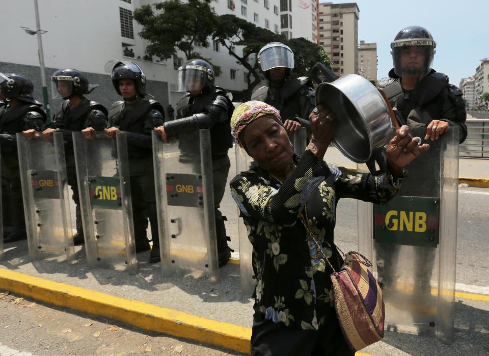 A woman bangs on a pot in front of Bolivarian National Guardmen blocking a road to prevent demonstrators from arriving at the Food Ministry, in Caracas, Venezuela, Saturday, March 8, 2014. Venezuelans returned to the streets for the "empty pots march" to highlight growing frustration with shortages of some everyday items. In Caracas, the march was scheduled to end at the country's Food Ministry, but the evening before Caracas' mayor announced that he had not authorized the march. (AP Photo/Fernando Llano)