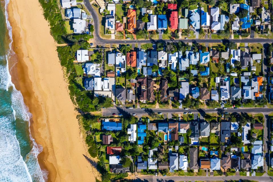 An aerial view of dozens of homes and the beach in a coastal suburb.