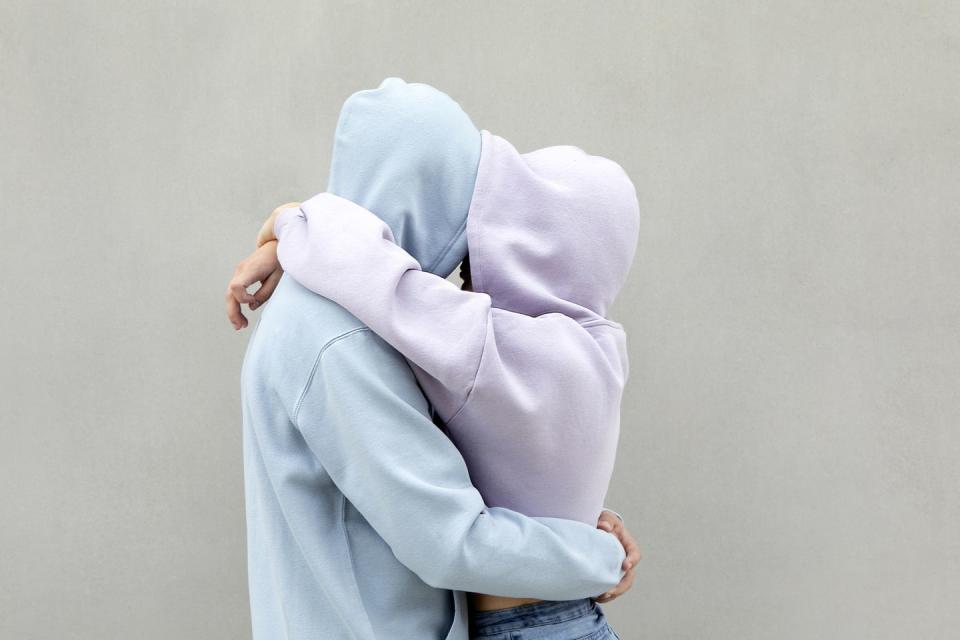 couple in hooded shirt embracing each other by wall