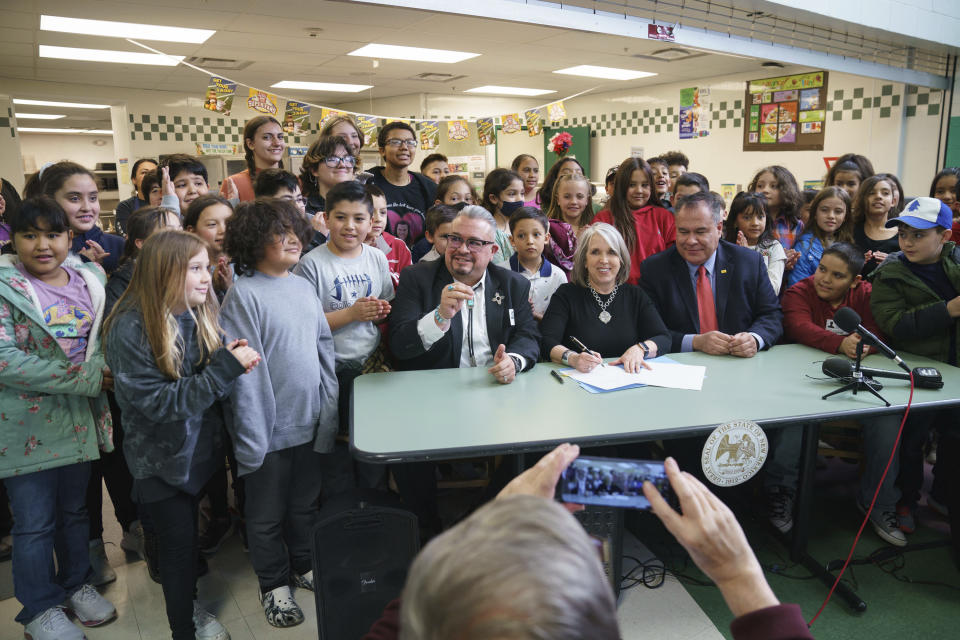 In this image provided by Gov. Michelle Lujan Grisham's office, the Democratic governor, center, signs a bill during a celebration with sponsors Sens. Michael Padilla, right, and Leo Jaramillo, left, at Pinon Elementary School in Santa Fe, N.M., Monday, March 27, 2023. The legislation provides universal free school meals for New Mexico students. (David Lienemann/Office of the Governor via AP)