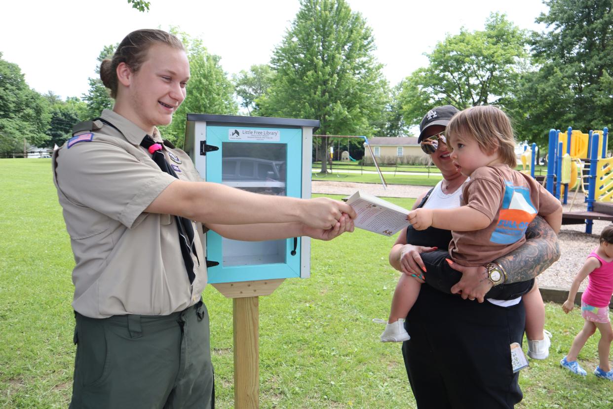 Boy Scout Ben Ehrhardt hands a book to a child at Meadowbrook Lake Park in front of the Little Free Library he built there.