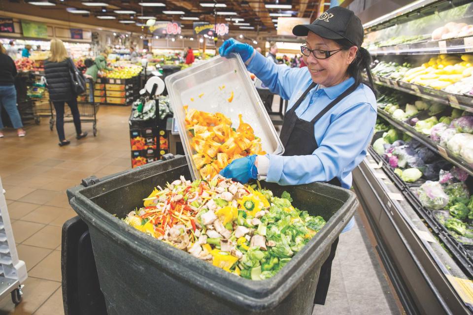 A Wegmans worker puts food into a compost bin.