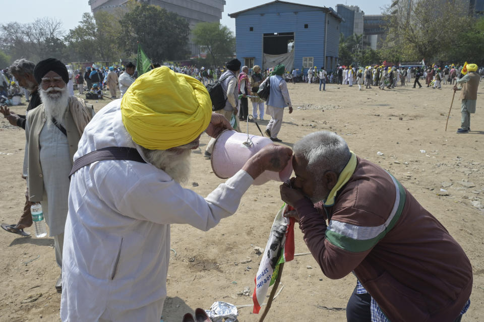 A farmer offers drinking water to another as Indian farmers who have been protesting to demand guaranteed crop prices gather at Ramlila ground in New Delhi, India, Thursday, March 14, 2024. (AP Photo)