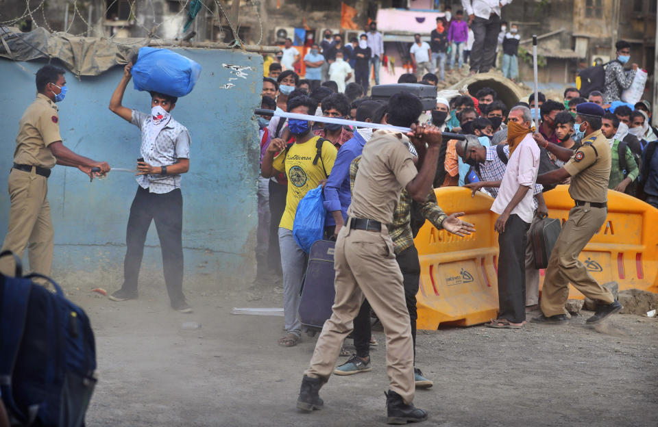 In this Friday, May 15, 2020, photo, police officers try to control a crowd of migrant workers from other states gathering outside a railway station desperate to return to their homes, in Mumbai, India. Tens of thousands of impoverished migrant workers are on the move across India, walking on highways and railway tracks or riding trucks, buses and crowded trains in blazing heat amid threat to their lives from the coronavirus pandemic. (AP Photo/Rafiq Maqbool)