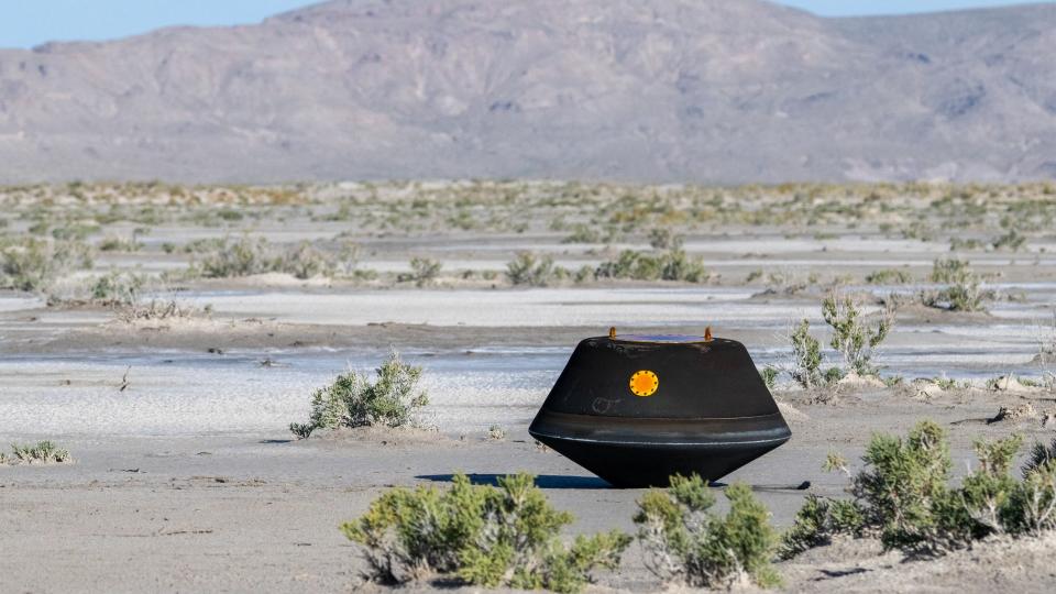 A black hexagona box with an orange eye in the center, sitting in the Utah desert. This is the OSIRIS-REx return capsule, safely landed on Earth