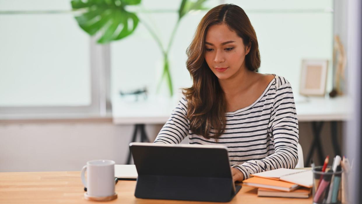 Photo of beautiful creative woman using a stylus pen to drawing on computer tablet with keyboard case that putting on working desk while sitting in orderly living room.