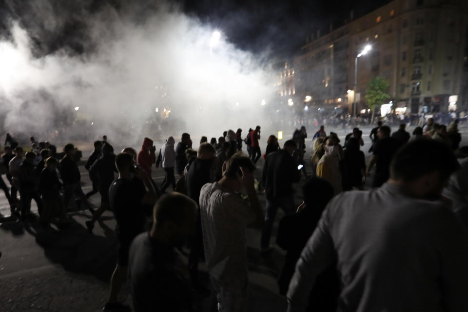 Protesters run from tear gas in front of Serbian parliament building in Belgrade, Serbia, Tuesday, July 7, 2020. Thousands of people protested the Serbian president's announcement that a lockdown will be reintroduced after the Balkan country reported its highest single-day death toll from the coronavirus Tuesday. (AP Photo/Darko Vojinovic)