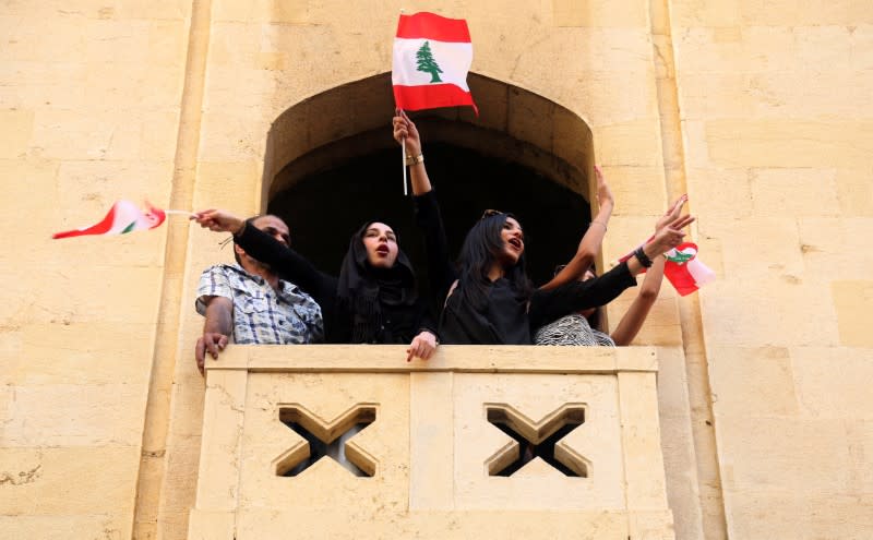 Women hold Lebanese flags as they stand on a balcony during a protest targeting the government over an economic crisis, in Beirut