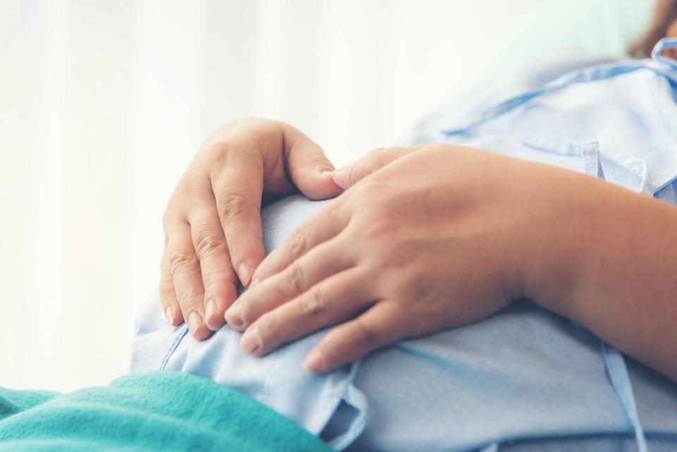 A pregnant woman holds her stomach while wearing a hospital gown