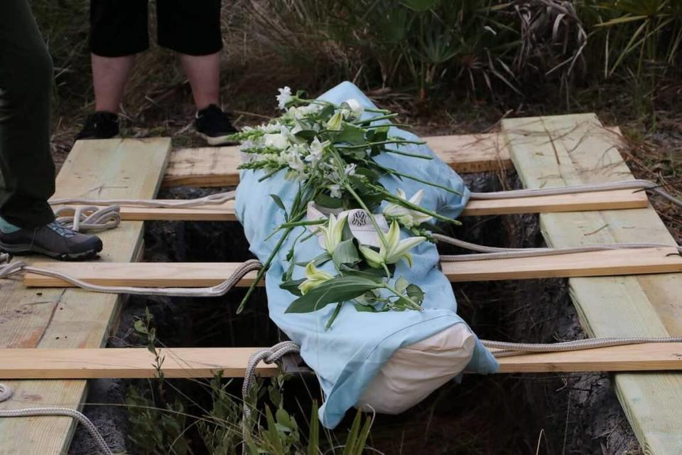 A body wrapped in a burial shroud is covered in flowers before being lowered into a grave at Heartwood Preserve Conservation Cemetery near Tampa, Florida.