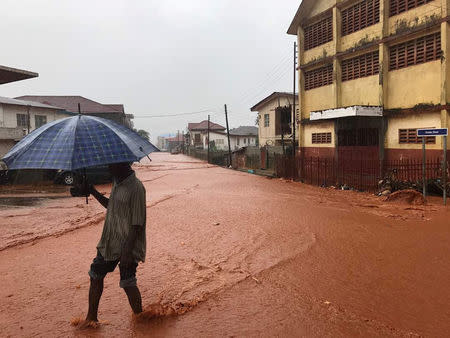 A man walks under umbrella in water covered street in Freetown, Sierra Leone August 14, 2017 in this picture obtained from social media. Instagram/dawncharris via REUTERS