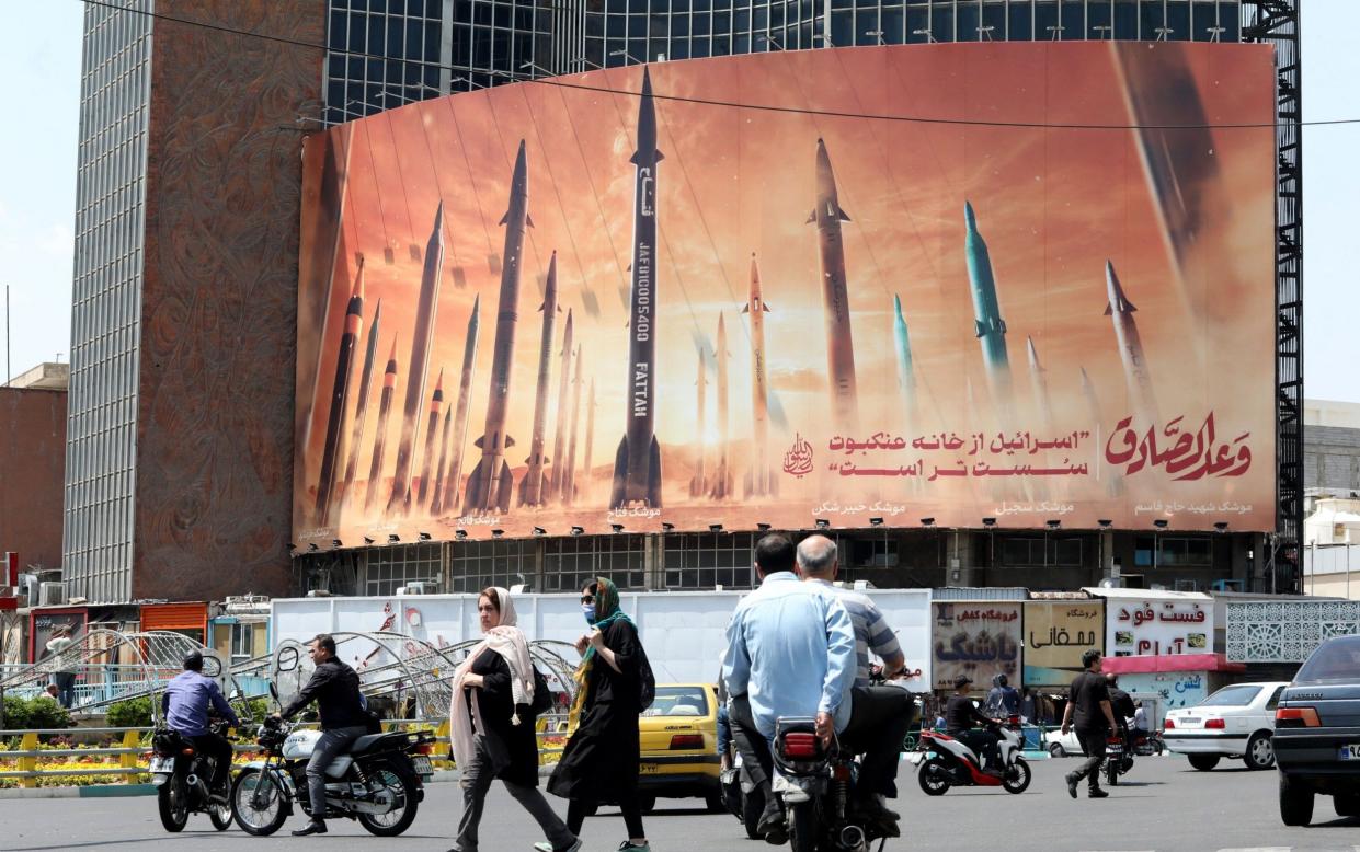 Motorists drive their vehicles past a billboard depicting Iranian missiles in Tehran on April 20