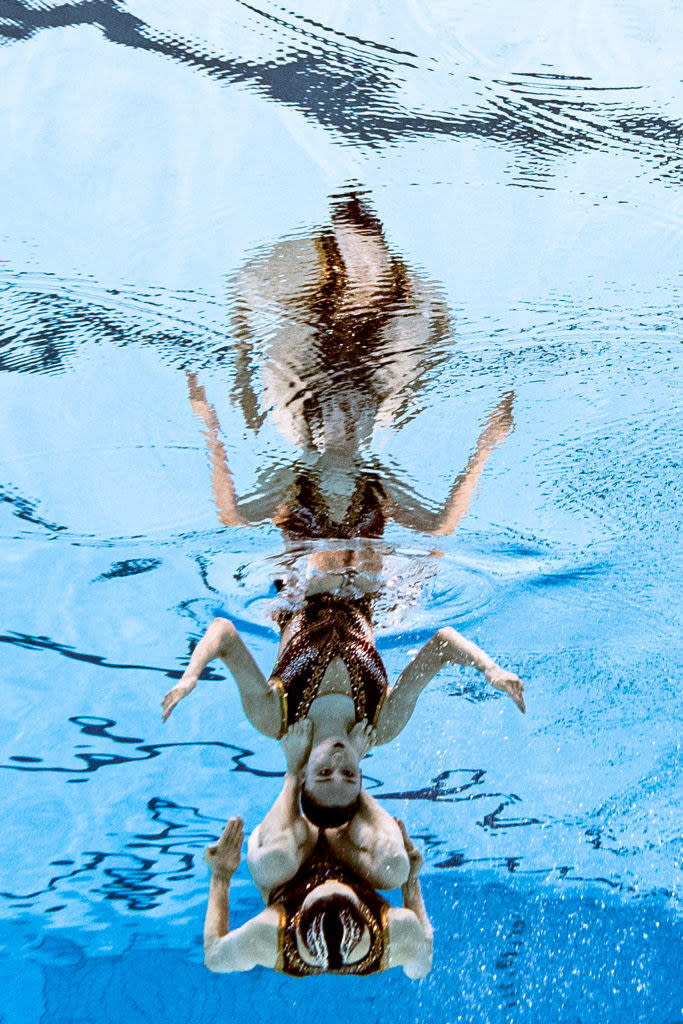 Two swimmers stacked on each other and upside down while underwater