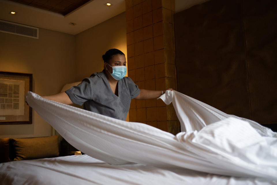 A hotel maid changes the sheets on a bed.