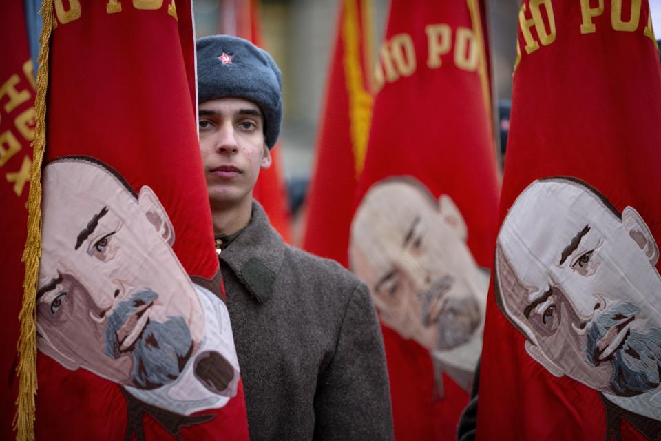 A Russian soldier dressed in Red Army World War II winter uniform stands amid Soviet-era flags as he waits to take part in a reconstruction of a World War II-era parade in Moscow's Red Square, Russia, Thursday, Nov. 7, 2019. The Nov. 7, 1941 parade saw Red Army soldiers move directly to the front line in the Battle of Moscow, becoming a symbol of Soviet valor and tenacity in the face of overwhelming odds. (AP Photo/Alexander Zemlianichenko)