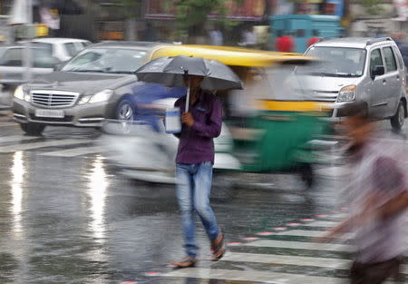 A man holds an umbrella and a teapot as he walks through a busy road during a rain shower in Ahmedabad, June 24, 2015. REUTERS/Amit Dave